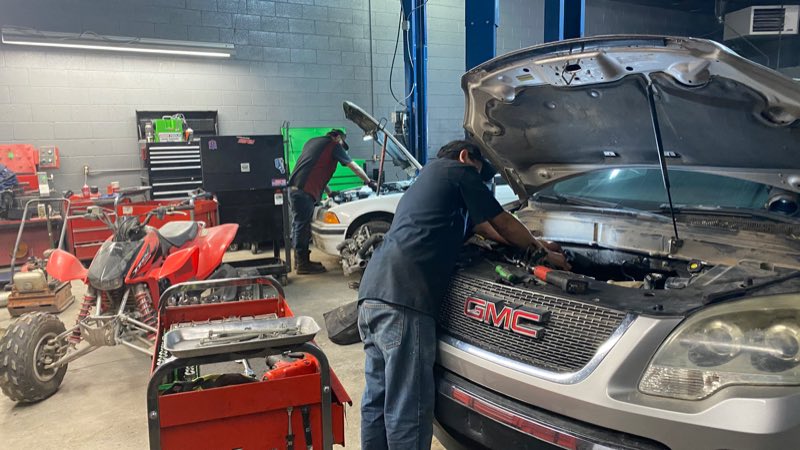 Technician working on a GMC with the hood up in the service bay